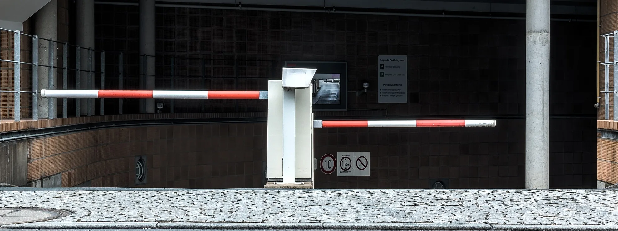 Entrada de um estacionamento com dois braços de cancela e sua coluna de controle